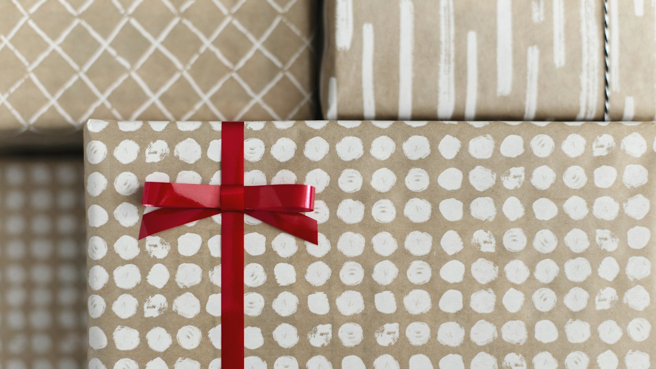 A wrapped gift box with a red ribbon bow resting against patterned cushions